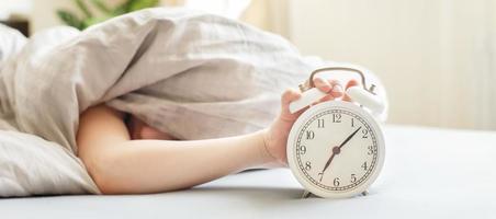 boy lying on the bed and stopping alarm clock in morning. childs hand reaching for the alarm clock to turn it off. photo