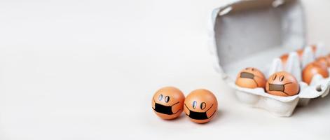 chicken eggs with drawn medical mask with egg carton on white background. Easter eggs holidays decoration. banner photo