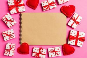 Top view of craft notebook surrounded with hearts and gift boxes on colorful background. Valentine's day photo