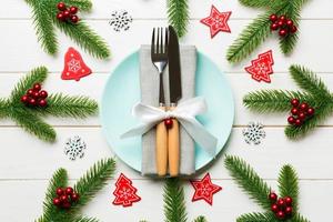 Top view of cutlery and plate on festive wooden background. New Year family dinner concept. Fir tree and Christmas decorations photo