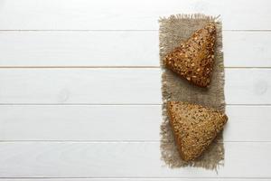 Several small multi grain triangular shaped bread sprinkled with whole sunflower seeds, flax and sesame seeds on a sackcloth photo