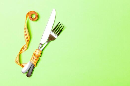 Top view composition of fork and knife wrapped in measuring tape on green background with empty space for your ideas. Overweight and overeating concept photo