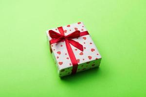 Valentine or other holiday handmade present in paper with red hearts and gifts box in holiday wrapper. Present box of gift on green colored table top view with copy space, empty space for design photo