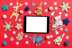 Top view of digital tablet, holiday toys and decorations on red Christmas background. New Year time concept photo