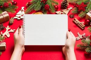 Top view of female hand making some notes in noteebok on red background. New Year decorations and toys. Christmas time concept photo