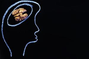 silueta de persona cabeza dibujada con cerebro de abstracción en forma de nuez sobre fondo negro. comida saludable para pensar. foto