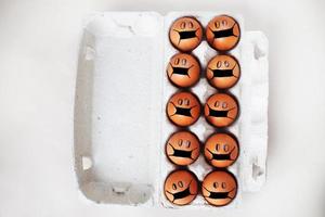 chicken eggs with drawn medical mask on egg carton on white background. Easter eggs holidays decoration. photo