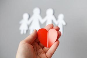 hand holding red heart on background of paper cut family photo