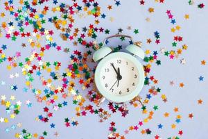 Alarm clock showing five minutes to twelve on a purple background with milticolored sequins photo