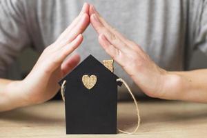 womans hand covered little toy house. Home insurance concept photo