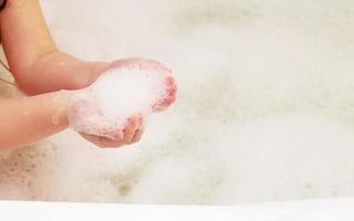 little baby girl playing with foam in bath tub. photo