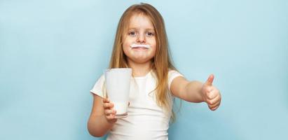 little beautiful girl holding milk in glass on a blue background. child drinks yogurt. banner photo