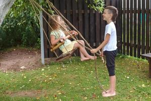 niño y niña montan en un columpio en el pueblo. hermano juega con su hermana foto