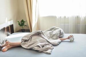 boy lying on the bed and stopping alarm clock in morning. childs hand reaching for the alarm clock to turn it off. photo