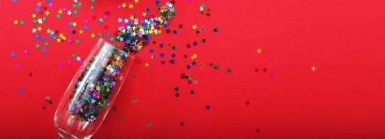 Champagne glass with star shaped sequins on a red background. banner. Party, christmas, new year, concept. photo