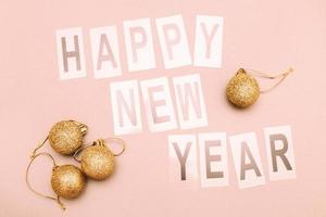 The inscription happy new year with shiny Christmas toy balls on a pink background photo