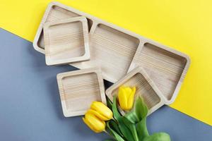 platos vacíos de madera para merienda y flores sobre fondo de color gris y amarillo foto