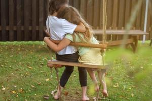 children sitting on a swing in the garden. older brother hugging little sister photo
