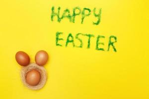 inscription happy easter from grass with bunny eggs and nest on yellow background photo