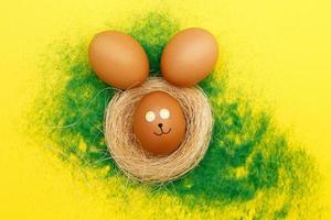 happy easter bunny eggs in nest on the decorative grass on yellow background. copy space for text photo