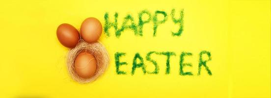 inscription happy easter from grass with bunny eggs and nest on yellow background photo