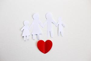 Happy paper cut family holding hands on a light wooden background with red heart. photo