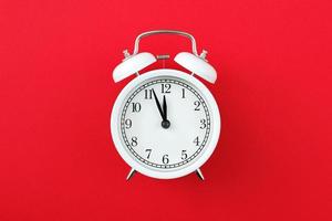 Alarm clock showing five minutes to twelve on a red background. Copy space photo