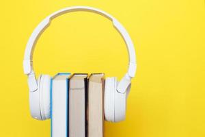 concepto de libro de audio con auriculares blancos modernos y libro de tapa dura sobre un fondo amarillo. escuchando un libro. foto