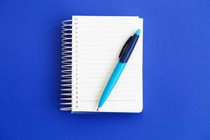 Top view of blank note paper with pen on blue background photo