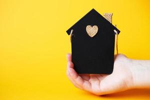 womans hand holding little toy house made of chalk board on a orange background. photo