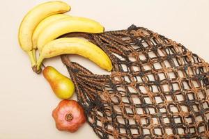 brown string bag with ripe fruits on a beige background photo