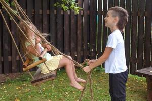 niño y niña montan en un columpio en el pueblo. hermano juega con su hermana foto