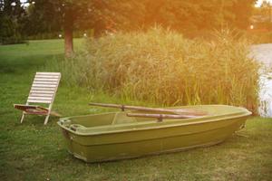 sillón de madera y un bote en la hierba de la orilla del lago tranquilo foto