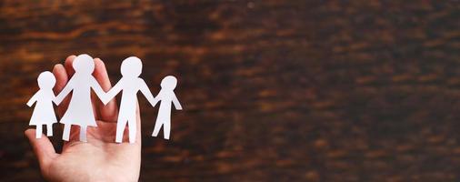 human hand holding happy paper cut family on a brown wooden background photo