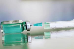 Vial filled with liquid vaccine in medical lab with syringe. medical ampoule and syringe on the glass surface photo