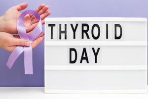 inscripción día internacional de la tiroides, cinta violeta y mano de mujer sosteniendo una carta sobre fondo morado foto