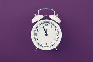 Alarm clock showing five minutes to twelve on a purple background. photo