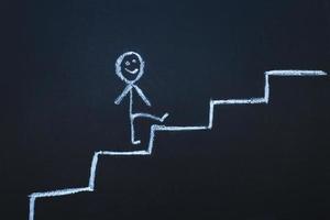 drawn man on the chalk board climbs up step by step to the top of career stairs. copy space photo