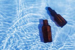 Brown glass oil bottle under fresh water on a blue background. Aromatherapy and perfumes concept photo