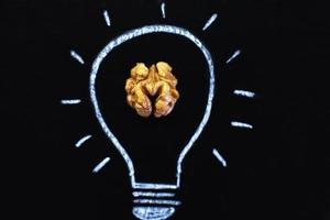 Light bulb with tasty shelled walnut on black background photo