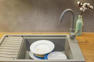 Pile of dirty dishes like plates in the grey modern granite sink in the kitchen photo