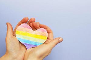 hands holding lgtb flag in the form of a heart on a purple backgroubd photo