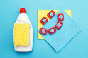 cápsulas para lavavajillas, detergente líquido para lavavajillas, trapo de cocina y esponjas sobre un fondo azul. foto