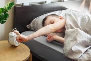 boy lying on the bed and stopping alarm clock in morning. childs hand reaching for the alarm clock to turn it off. photo