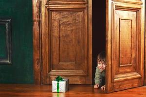 child boy peeks out of the door with a christmas gift box. photo