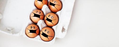 chicken eggs with drawn medical mask on egg carton on white background. Easter eggs holidays decoration. banner photo