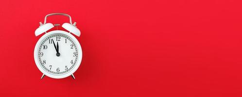 Alarm clock showing five minutes to twelve on a red background. Copy space. banner photo