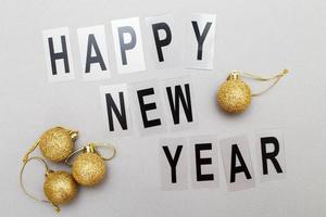 The inscription happy new year with shiny golden Christmas toy balls on a grey background photo