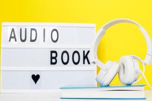 concepto de libro de audio con auriculares blancos modernos y libro de tapa dura sobre un fondo amarillo. inscripción en una caja de luz foto