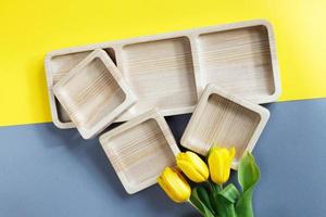 platos vacíos de madera para merienda y flores sobre fondo de color gris y amarillo foto